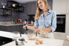 Mulher sorridente usando uma jarra medidora KitchenAid de 2 litros enquanto prepara uma receita na cozinha.