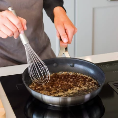 Pessoa usando um fouet de aço inox para misturar ingredientes em uma panela.