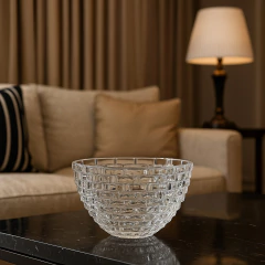 Centro de mesa de vidro transparente em formato arredondado, com detalhes em camadas, sobre uma mesa escura em ambiente aconchegante.