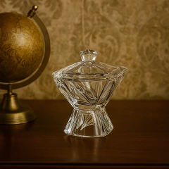 Bomboniere potiche de vidro transparente com tampa e pé, design facetado, sobre mesa de madeira com globo antigo ao fundo