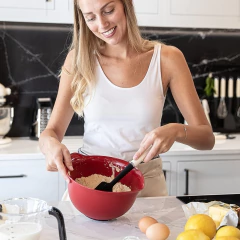 Mulher sorridente misturando ingredientes em uma tigela vermelha com uma espátula de silicone KitchenAid.
