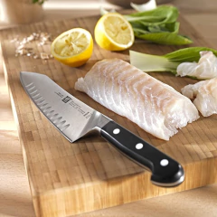 faca santoku com cabo sintético preto e lâmina gravada com a marca ao lado de um pedaço de peixe