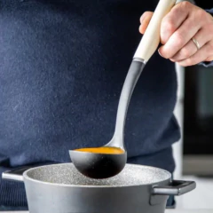 Concha de nylon preta com cabo branco sendo utilizada para servir sopa de uma panela