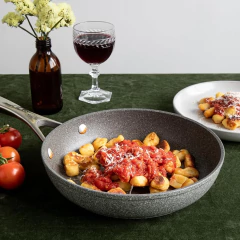 Frigideira antiaderente com gnocchi ao molho de tomate, acompanhada de uma taça de vinho e tomates frescos.