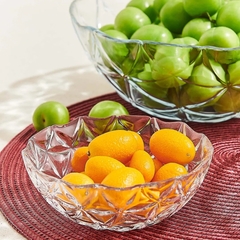 Conjunto de duas tigelas de vidro, uma com frutas laranjas e outra com uvas verdes, sobre uma toalha de mesa vermelha.