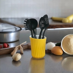 Porta utensílios de cerâmica amarelo com talheres de cozinha pretos em uma bancada de cozinha moderna.