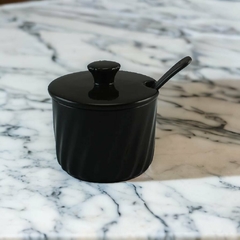Açucareiro preto com colher de cerâmica, sobre uma mesa de mármore.