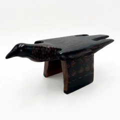 Escultura indígena de madeira representando um pássaro, com detalhes em pintura tradicional Mehinaku, em tons escuros e desenhos geométricos