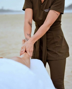 Profissional usando scrub Cíntia conforto marrom realizando massagem em uma perna na praia
