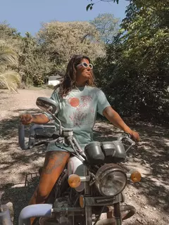 Mujer con remerrón Santa Teresa, sentada en una moto, rodeada de naturaleza.