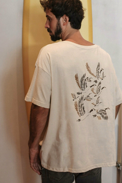 Hombre de espaldas vistiendo un remerón color beige con un diseño de pájaros en la espalda.