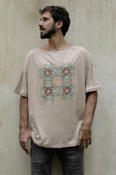 Hombre posando con un remerón beige con estampado colorido en el pecho, frente a un fondo claro.