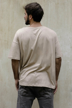 Hombre de espaldas vistiendo un remerón beige, con un fondo de pared clara.