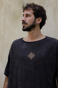 Hombre usando un remerón negro con un diseño de mosaico en el pecho, de perfil, frente a un fondo claro.