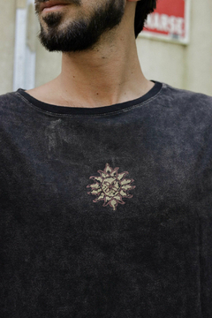 Hombre usando un remerón negro con un diseño de sol en el pecho, parte de la colección 2024.