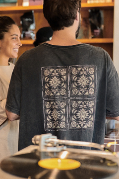 Hombre de espaldas usando un remerón gris con estampado de mosaico en la parte posterior, en un entorno de tienda.