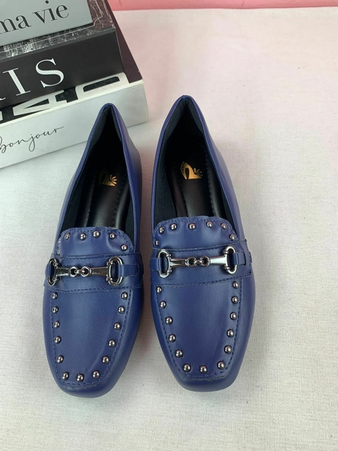 Mocassim bico quadrado azul com detalhes em tachinhas, exibido em fundo neutro.