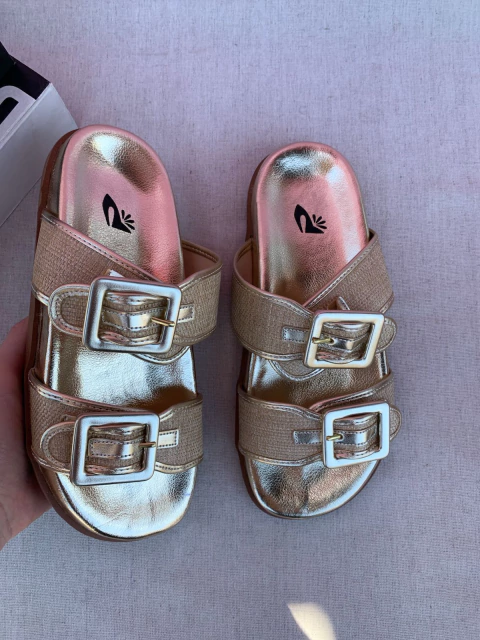Sandália slide dourada com duas fivelas grandes na parte superior, design moderno e sola flatform.