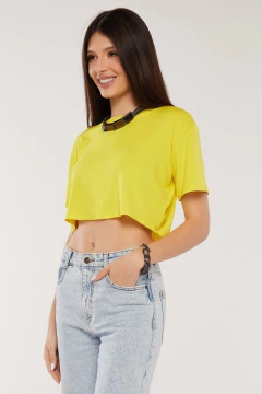 Modelo morena usando um cropped liso feminino amarelo em viscolycra, sorrindo, olhando para direita, mão esquerda no bolso da calça, sobre fundo branco. G&B Bros
