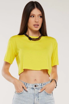 Modelo morena usando um cropped liso feminino amarelo em viscolycra, olhando para esquerda, mãos nos bolsos da calça, sobre fundo branco. G&B Bros