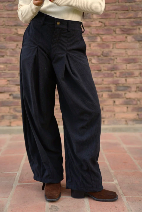 Pantalón Baggy de corderoy negro con corte amplio y pliegues delanteros, combinado con botas marrones de tacón bajo.