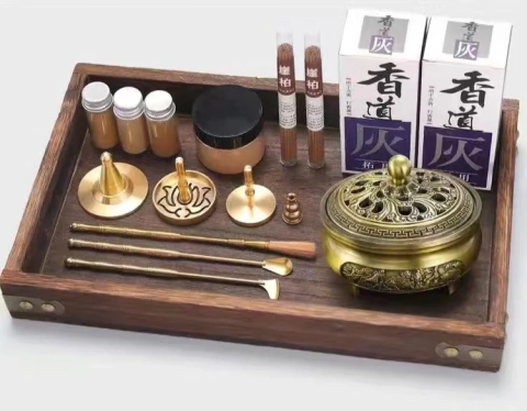 Conjunto de cerimonial de incenso para aromaterapia com queimador de metal dourado, acessórios em metal, frascos com pó e caixas de incenso, tudo disposto em uma bandeja de madeira escura.