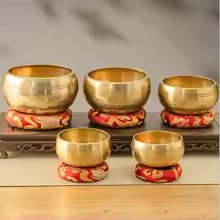 Conjunto de 5 tigelas tibetanas cantantes em diferentes tamanhos, cada uma apoiada em almofadas vermelhas decorativas