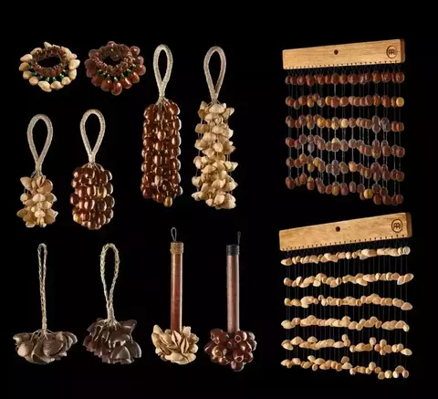 Vários instrumentos de percussão feitos com castanhas e sementes, como caxixis, chocalhos e pulseiras, dispostos sobre um fundo preto.