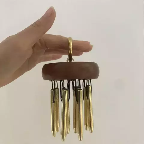 Um sino de pinos energéticos com uma base de madeira e pendentes dourados, sendo segurado por uma mão.