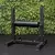 Banco regulable para sentadilla búlgara sobre piso de goma, con fondo de pared verde de hojas artificiales. Equipo de gimnasio ideal para entrenamiento de piernas.