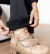 Detalhe de uma calça flare térmica preta sendo ajustada sobre uma bota bege com correntes, destacando o tecido e acabamento da peça.