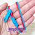 Foto: Pulseira zíper de plástico com uma faixa vermelha e outra azul celeste.