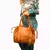 Mulher segurando uma bolsa de couro legítimo na cor caramelo, com alças práticas e um design elegante.