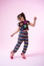 Menina usando um conjunto colorido com blusa de flores e calça xadrez, em fundo rosa.