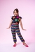 Menina sorridente vestindo um conjunto colorido com blusa de flores e calça xadrez em fundo rosa.