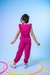 Menina usando um macacão rosa com detalhes de babados, de costas, em um fundo azul claro.