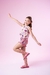 Menina sorrindo vestindo um conjunto infantil colorido com estampa de elefantes, posando em um fundo rosa.