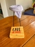 Coador de café individual com estampa "Café da Mamãe", apoiado em uma base de madeira, sobre uma mesa de madeira.