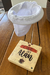 Coador de café individual personalizado com nome "Café do Alan" em uma base de madeira.