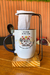 Caneca com ilustração de duas galinhas, texto "Tem amizade que vale a pena" e suporte para coar, em uma mesa de madeira.