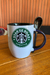 Caneca branca com logotipo "Star de Boas" e colher na alça, sobre uma mesa de madeira.