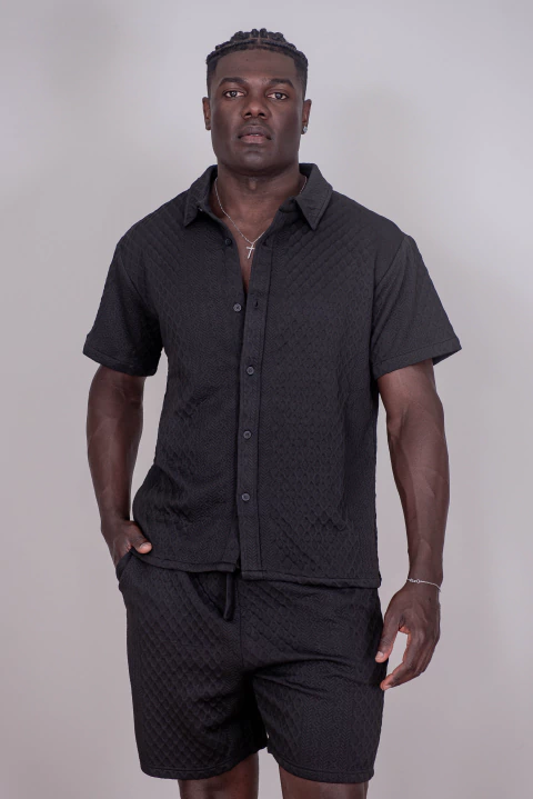 Homem vestindo conjunto 5D preto com camisa de manga curta e bermuda texturizada, da Coleção Nova.