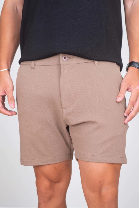 Short de alfaiataria masculino na cor caqui com cós meio elástico, detalhe de botão e bolsos, modelo vestindo peça.