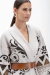 Mulher usando cardigan branco com detalhes em preto e marrom, com cinto largo na cintura, aparência elegante e moderna.
