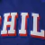 Detalhe em close das letras bordadas "PHIL" na camisa azul do Philadelphia 76ers