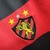 Emblema do kit infantil Umbro 23/24, apresentando um leão em destaque, estrelas e listras vermelhas e pretas.