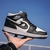 Um tênis de basquete unissex nas cores preto e branco, com o logo da Nike e detalhes clássicos, sendo segurado por uma mão ao ar livre.