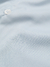 Close-up de uma camisa boxy azul, destacando um botão branco e a textura do tecido.