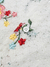 Detalhe de uma camisa de renda floral, destacando bordados coloridos e um botão branco.