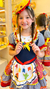 Menina sorrindo vestindo um vestido de quadrilha infanto juvenil, com detalhes coloridos e chapéu decorado, pronta para festa junina.